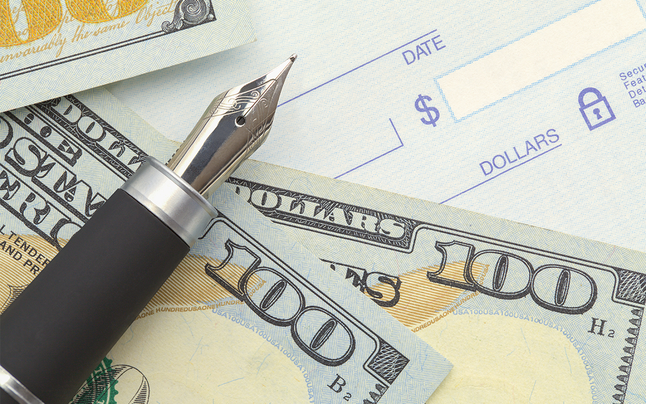 A blank check and two hindered dollar bills are shown that are typically found in a check cashing business for sale.
