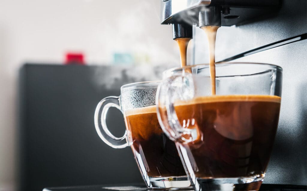 Two glass cups getting filled with hot espresso from a coffee machine that is typically found in a coffee business.