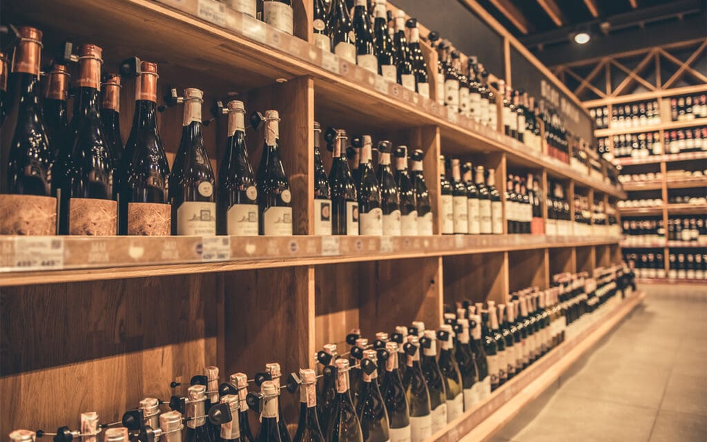 Multiple wooden shelves stocked full of bottles of wine and liquor that can be found in a liquor store for sale.