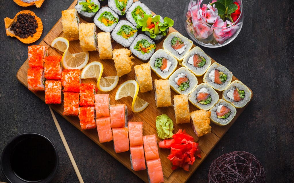 Assortment of sushi rolls with ginger, wasabi and lemon slices that can be found in a sushi restaurant for sale.