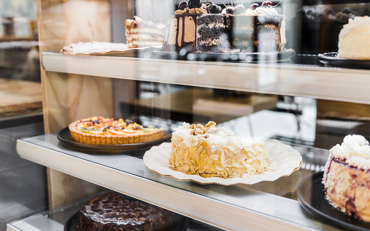 Different types of cakes displayed in a display case that can be found in a franchise bakery business displayed for sale.