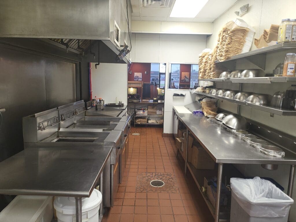 Kitchen that can be found in a typical restaurant for sale that includes stainless steel tables, fryers, a grill and more.